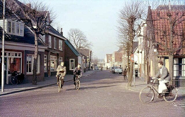 Gezicht op de Deutzstraat gezien vanaf het Kerkplein. Situatie januari 1961. Fietsers v.l.n.r.: Joop Walgreen, Wim van der Moolen (scholieren) en rechts Cees Huipen (schilder). (dia C. Duineveld)